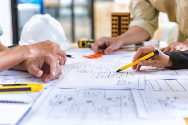 Image of three people around a table looking at building floor plans, representing an architectural workshop.
