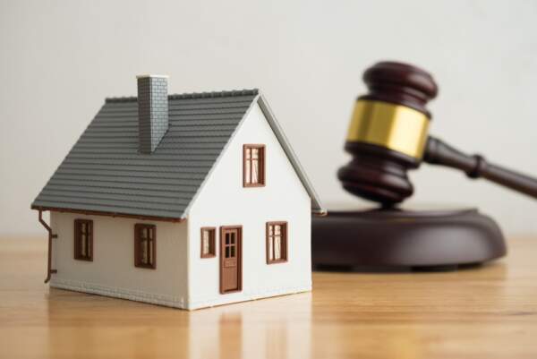 A model house placed next to a judge's gavel, symbolising building regulations and legal compliance.