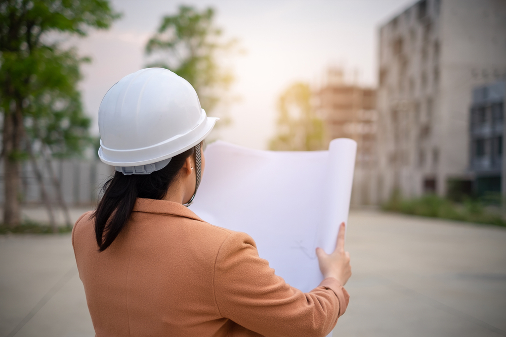 Photo of a principal designer reviewing building plans while visiting a construction site.